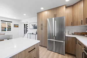 Kitchen featuring freestanding refrigerator, light wood-style floors, recessed lighting, and light stone counters