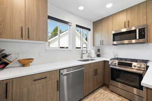 Kitchen featuring stainless steel appliances, a sink, recessed lighting, light stone counters, and light wood-style flooring