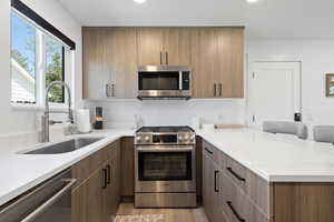 Kitchen with appliances with stainless steel finishes, a sink, a peninsula, light wood-style floors, and light stone counters