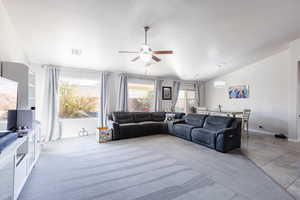 Living area with light tile patterned floors, visible vents, baseboards, vaulted ceiling, and ceiling fan with notable chandelier