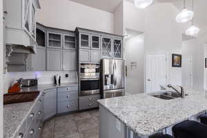 Kitchen featuring gray cabinets, stainless steel appliances, backsplash, a sink, and a kitchen breakfast bar