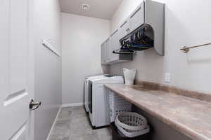 Clothes washing area featuring baseboards, visible vents, washer and dryer, and cabinet space