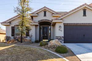 View of front of home featuring a garage, stone siding, a tiled roof, concrete driveway, and stucco siding