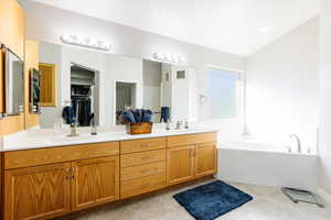 Primary bathroom featuring double vanity, a garden tub, lofted ceiling, and a sink