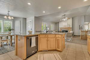 Kitchen featuring a sink, dishwashing machine, ceiling fan, a tiled fireplace, and open floor plan