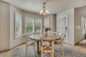 Dining space featuring light tile patterned flooring, a chandelier, baseboards, and a textured ceiling