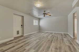 Unfurnished room with a textured ceiling, a ceiling fan, light wood finished floors, and baseboards