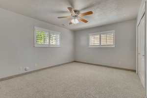 Unfurnished bedroom featuring multiple windows, a closet, a textured ceiling, carpet flooring, and a ceiling fan
