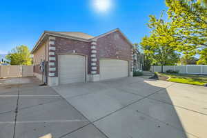 View of property exterior with brick siding, driveway, a gate, an attached garage, and fence