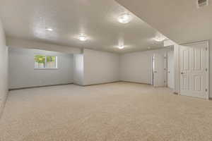 Empty room featuring a textured ceiling, light colored carpet, and baseboards