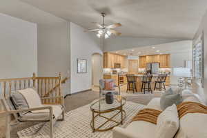 Living room featuring arched walkways, lofted ceiling, ceiling fan, light carpet, and baseboards