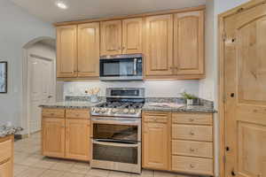 Kitchen featuring stainless steel appliances, light brown cabinets, light stone counters, arched walkways, and light tile patterned floors