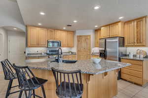 Kitchen featuring appliances with stainless steel finishes, light tile patterned floors, a textured ceiling, a sink, and light brown cabinets