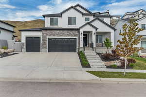 View of front of home with board and batten siding, concrete driveway, a gate, stone siding, and fence