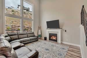Living area featuring light wood finished floors, a glass covered fireplace, a high ceiling, and baseboards