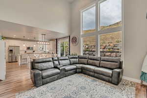 Living room with light wood-type flooring, baseboards, recessed lighting, and a high ceiling