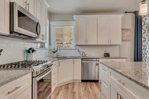 Kitchen featuring stainless steel appliances, a sink, light wood-type flooring, and white cabinetry