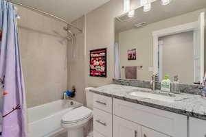 Bathroom featuring shower / tub combo, toilet, vanity, and a textured ceiling