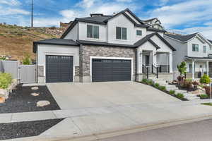 Modern inspired farmhouse featuring board and batten siding, a gate, stone siding, and concrete driveway