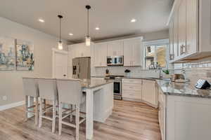 Kitchen with stainless steel appliances, light wood-type flooring, a breakfast bar, white cabinets, and recessed lighting