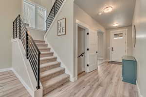 Entryway with light wood-style flooring, baseboards, stairway, and a textured ceiling