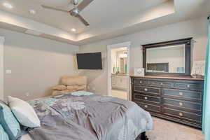 Bedroom with a raised ceiling, light carpet, ensuite bathroom, recessed lighting, and ceiling fan