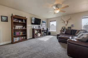 Carpeted living room featuring a ceiling fan and baseboards