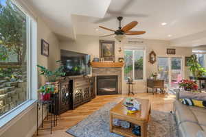 Living area with a glass covered fireplace, a ceiling fan, wood finished floors, recessed lighting, and baseboards