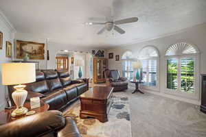Carpeted living room featuring arched walkways, ceiling fan, and ornamental molding