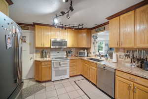 Kitchen featuring stainless steel appliances, a sink, light tile patterned floors, light stone counters, and crown molding
