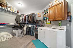 Upstairs Primary Suite Laundry area with washer and clothes dryer, cabinet space, light wood-type flooring, and a textured ceiling