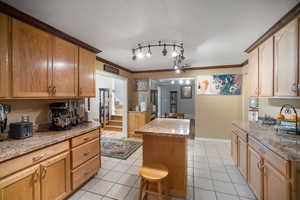 Kitchen featuring light tile patterned flooring, a center island, light stone counters, crown molding, and baseboards