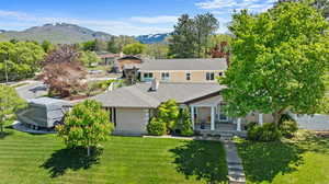 View of front of house featuring a front yard, covered porch, a mountain view, and a shingled roof
