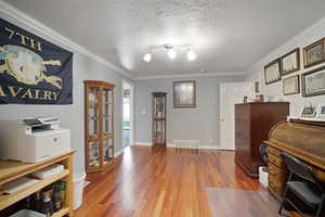 Office space featuring wood finished floors, crown molding, a textured ceiling, and baseboards
