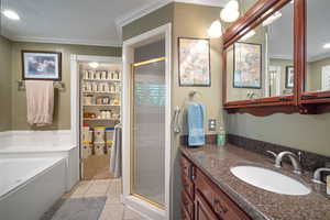Main floor Primary full bathroom featuring a shower stall, crown molding, vanity, tile patterned floors, and a bath