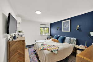 Bedroom with crown molding, a wall unit AC, and wood finished floors