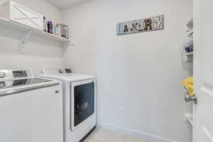 Laundry room with washer and dryer, light tile patterned flooring, and baseboards