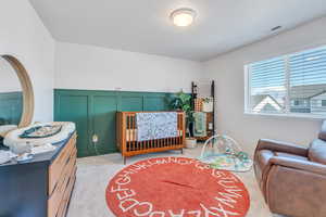 Bedroom with a decorative wall, light carpet, a crib, and wainscoting