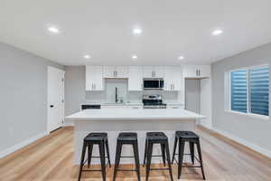 Kitchen featuring appliances with stainless steel finishes, a sink, a breakfast bar area, white cabinetry, and recessed lighting