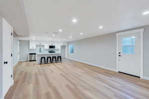 Unfurnished living room with a sink, baseboards, recessed lighting, light wood-style floors, and healthy amount of natural light