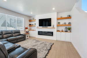 Living room featuring light wood-style flooring, a large fireplace, baseboards, recessed lighting, and a textured ceiling