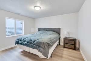 Bedroom with light wood-style flooring, a textured ceiling, and baseboards