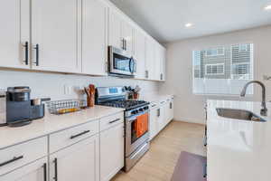 Kitchen with appliances with stainless steel finishes, a sink, white cabinets, baseboards, and light countertops