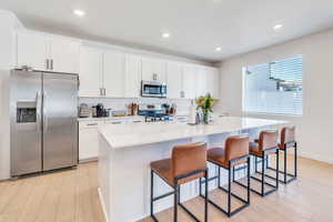 Kitchen with appliances with stainless steel finishes, light wood-style flooring, a breakfast bar, a center island, and white cabinetry