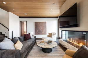 Living room with wooden ceiling, stairs, recessed lighting, wood finished floors, and a glass covered fireplace
