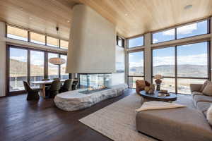 Living area with a mountain view, wood ceiling, a multi sided fireplace, healthy amount of natural light, and a towering ceiling