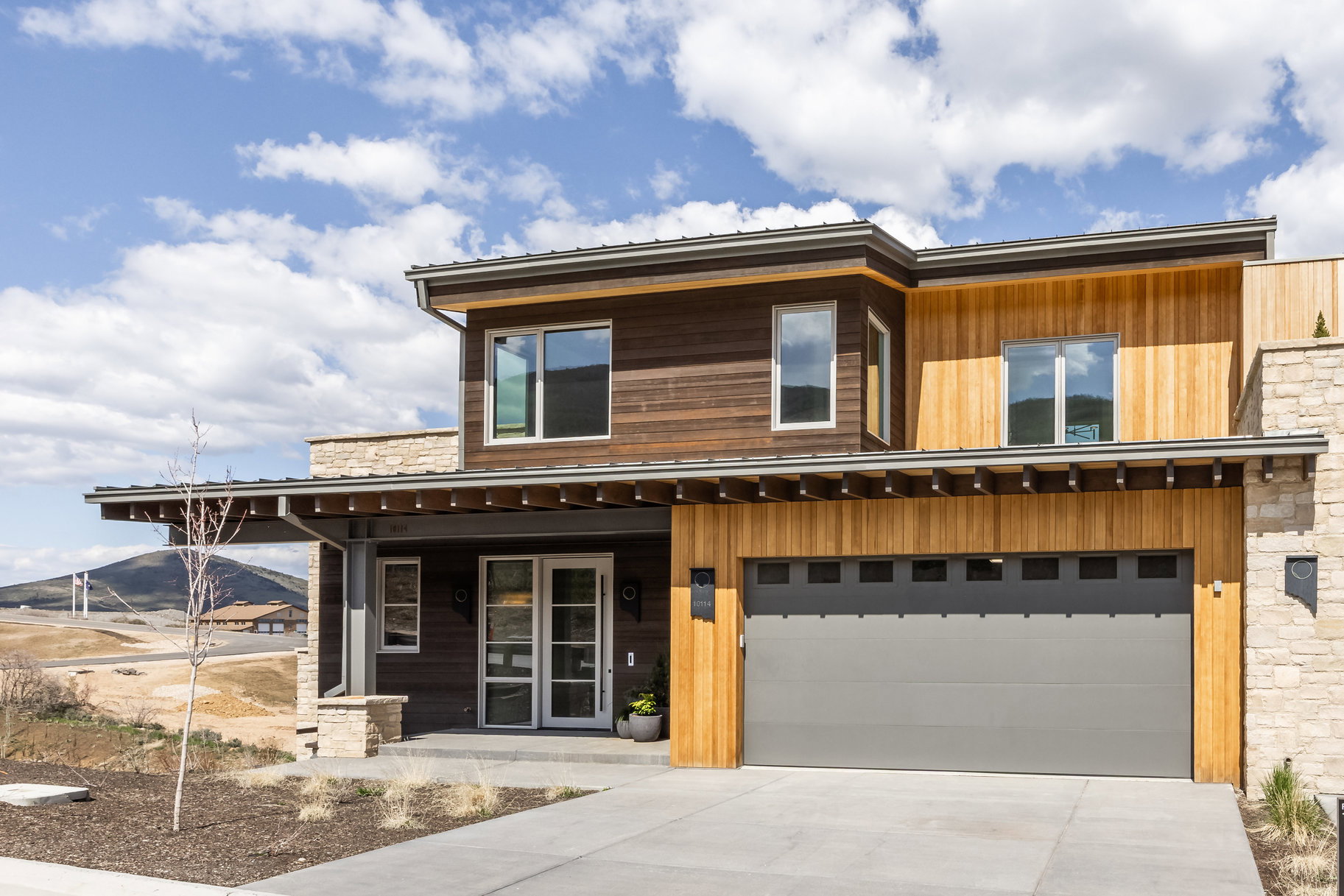 Contemporary home with a garage, concrete driveway, covered porch, and stone siding