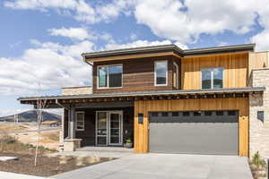 Contemporary home with a garage, concrete driveway, covered porch, and stone siding