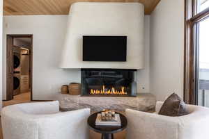 Carpeted living area featuring estacked washer and dryer, wood ceiling, and a glass covered fireplace