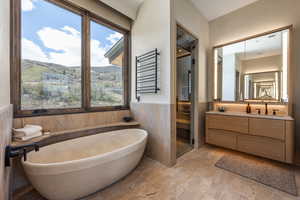 Bathroom featuring vanity, healthy amount of natural light, wainscoting, a freestanding tub, and a towel warmer